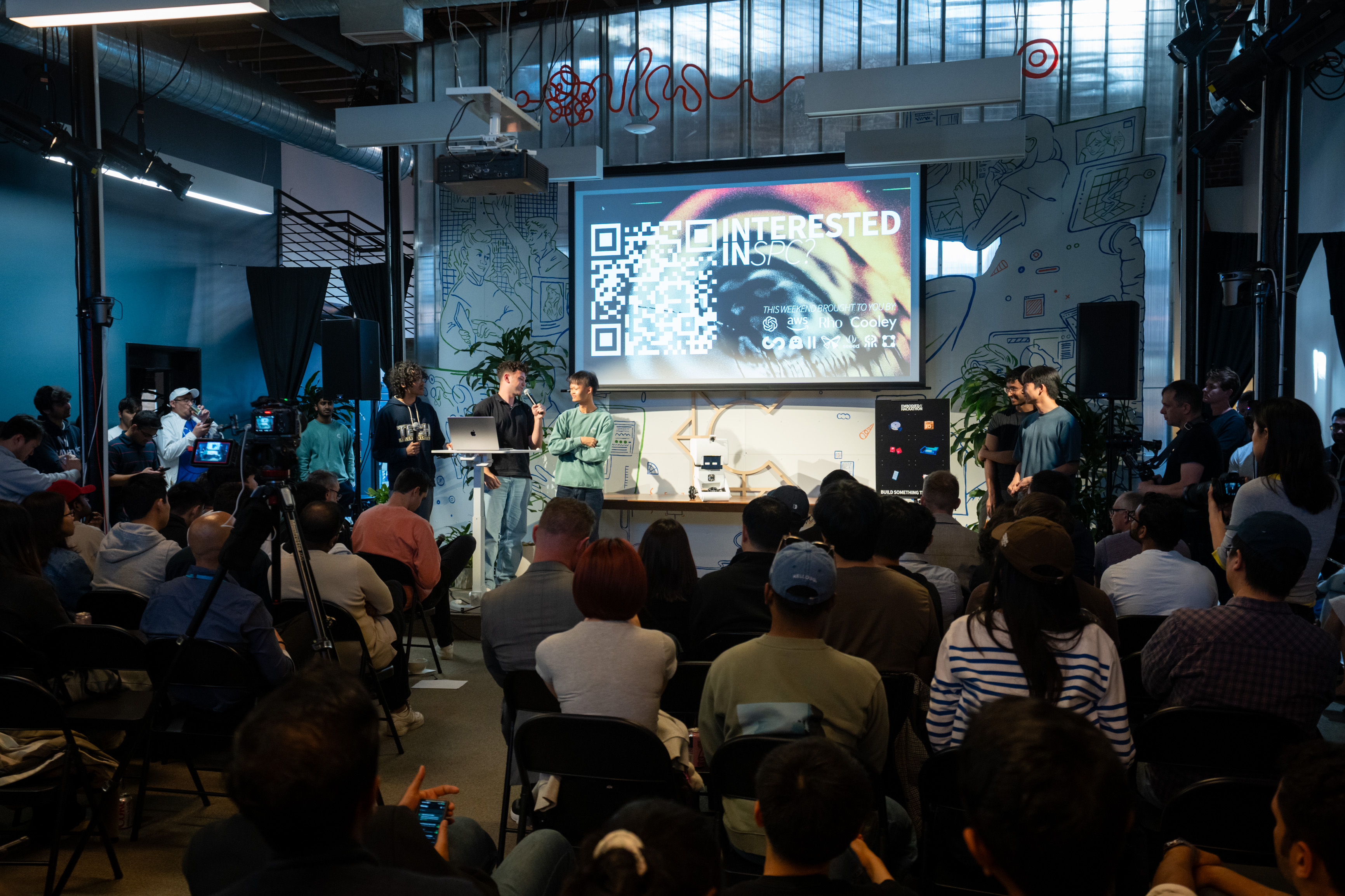 The MoBot team presenting on stage to a seated audience during the hackathon finals, with MoBot on a stand at the front
